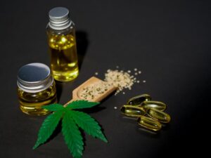 CBD oil bottles, gel capsules, hemp seeds on wooden spoon, and cannabis leaf arranged on dark background